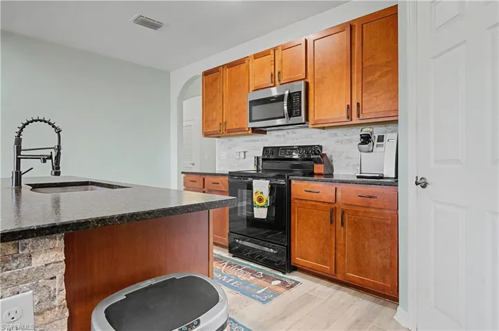 Kitchen featuring black / electric stove, arched walkways, stainless steel microwave, and brown cabinetry