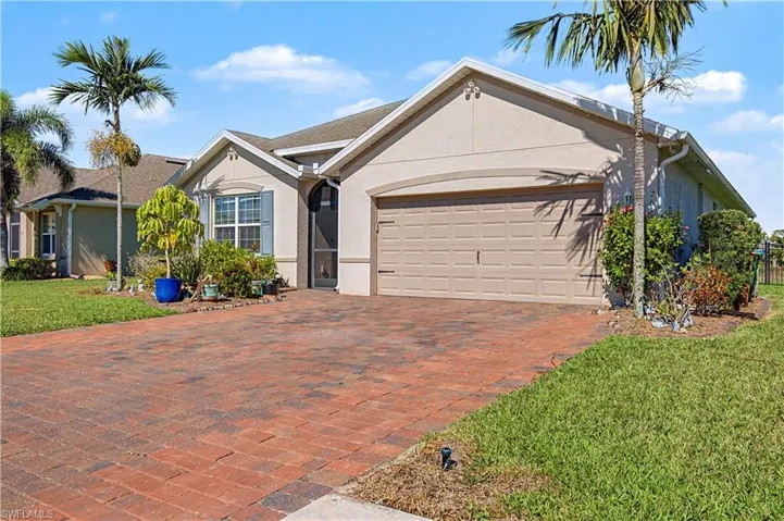 Ranch-style house with a front yard, stucco siding, paver driveway, and an attached garage