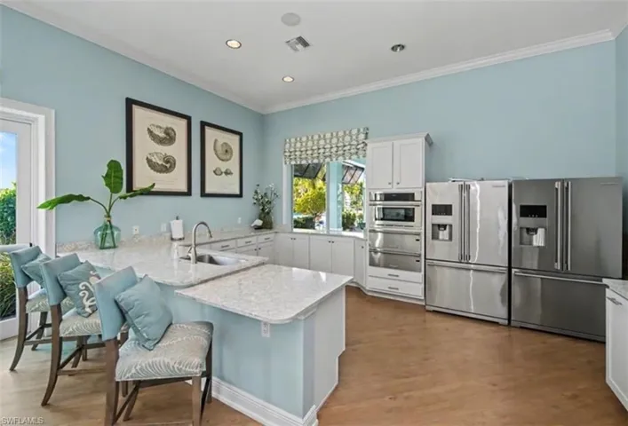 Community kitchen with stainless steel appliances, light stone counters, a kitchen bar, white cabinetry, and a peninsula