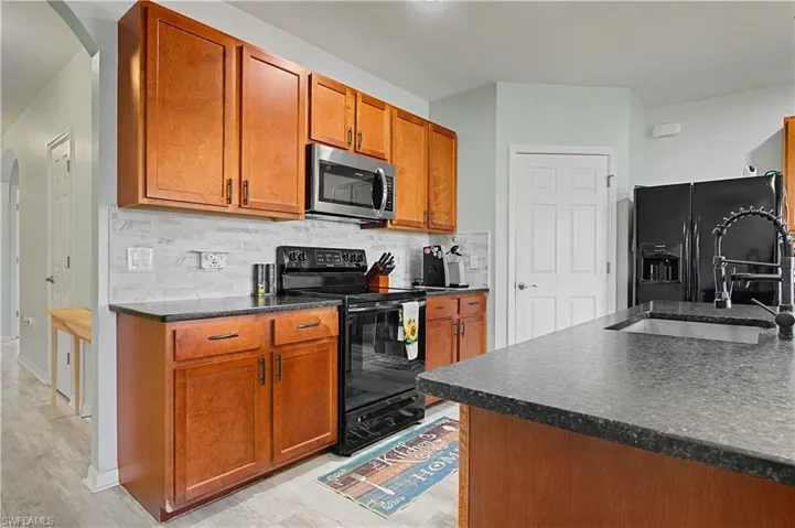 Kitchen with arched walkways, black appliances, brown cabinets, and backsplash