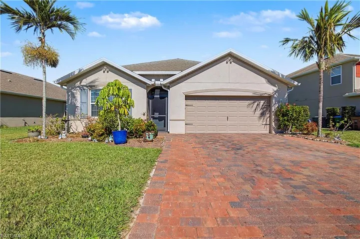 Ranch-style home featuring stucco siding, a front lawn, paver driveway, and an attached garage