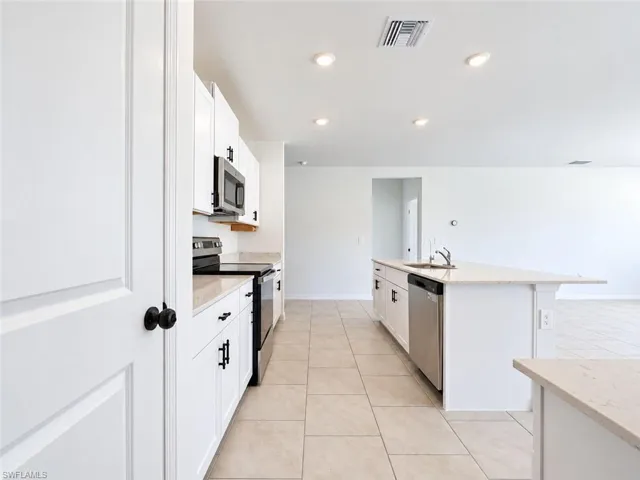 Kitchen featuring white cabinetry with dark hardware, stone-finish countertops, stainless steel appliances, a center island with a built-in sink, and tile flooring