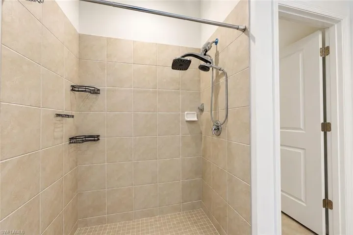 Shower enclosure featuring floor-to-ceiling tile, built-in metal corner shelving, a multi-function showerhead with integrated handheld sprayer, and a soap niche