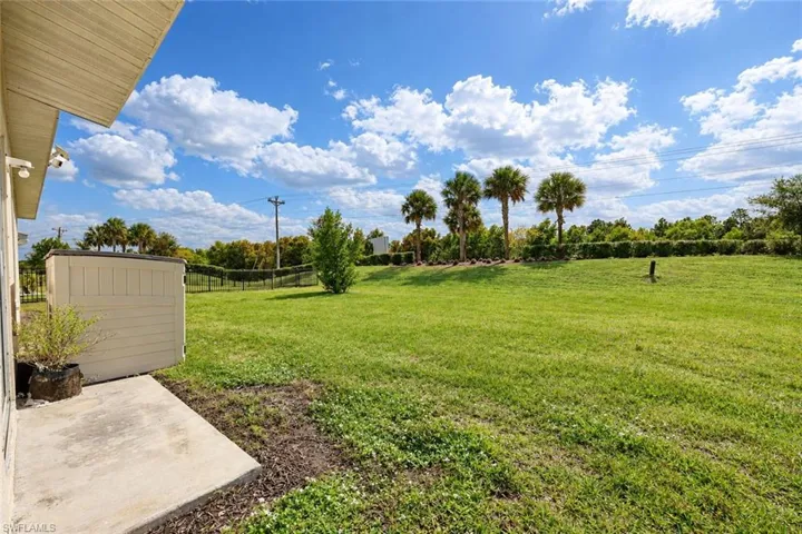 Expansive lawn with mature palm trees, perimeter fencing, and concrete patio area