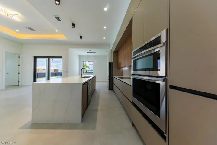 Kitchen featuring modern cabinets, double oven, a center island with sink, recessed lighting, and a raised ceiling