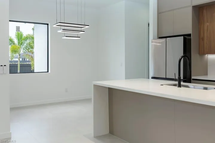 Kitchen with modern cabinets, freestanding refrigerator, hanging light fixtures, and light stone countertops