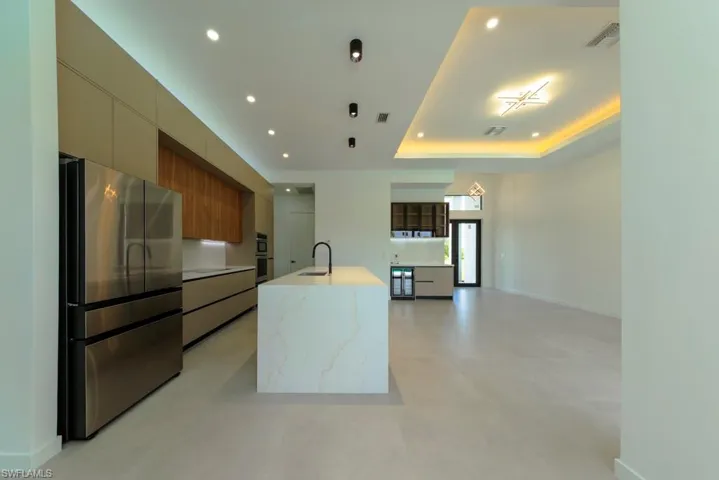 Kitchen featuring modern cabinets, stainless steel appliances, recessed lighting, a kitchen island with sink, and beverage cooler