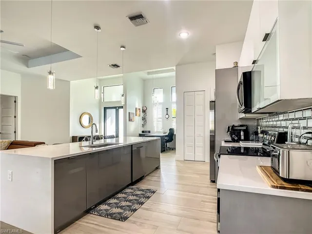 Kitchen with decorative light fixtures, modern cabinets, tasteful backsplash, an island with sink, and recessed lighting