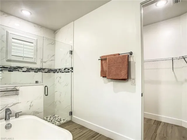 Bathroom with a marble finish shower, a walk in closet, wood finish floors, and recessed lighting
