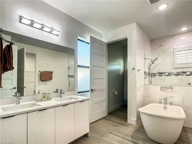 Full bath with double vanity, a freestanding bath, light wood-type flooring, a shower, and recessed lighting