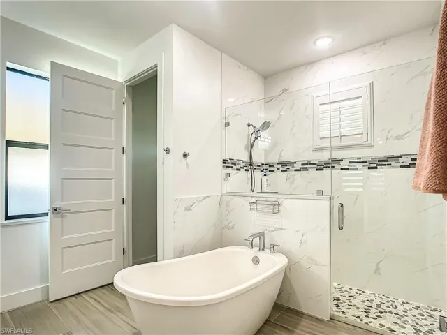 Bathroom featuring a marble finish shower, a freestanding bath, wood finish floors, plenty of natural light, and tile walls