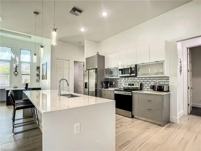 Kitchen featuring modern cabinets, hanging light fixtures, stainless steel appliances, a center island with sink, and recessed lighting