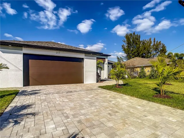 View of front facade with decorative driveway, stucco siding, a front lawn, and an attached garage