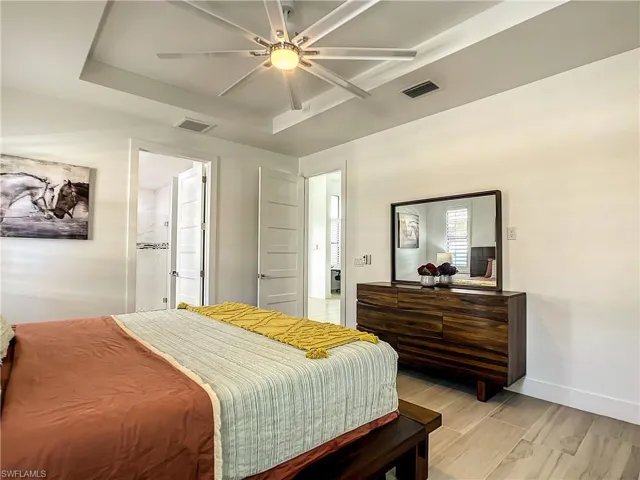 Bedroom with a raised ceiling, wood finish floors, ensuite bath, and ceiling fan