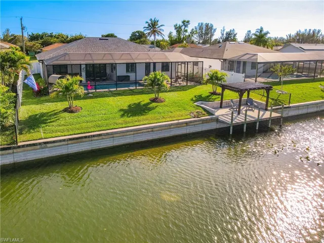 Back of property featuring a sunroom, a lawn, and a water view