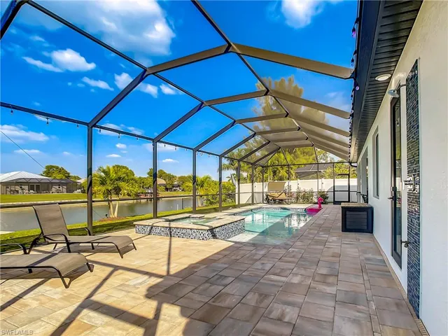 View of pool featuring a sunroom, a water view, a patio, a lanai, and a pool with connected hot tub