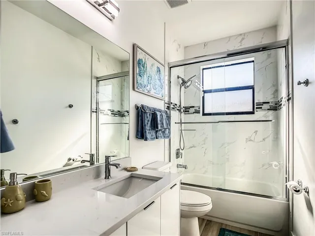 Full bathroom featuring combined bath / shower with glass door, vanity, and wood finished floors