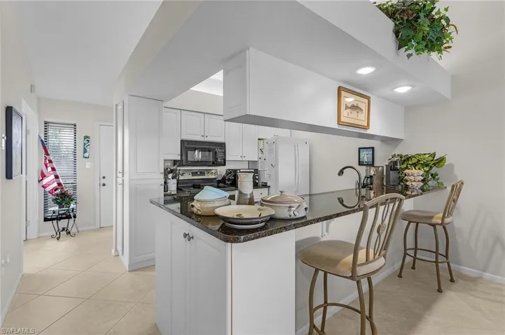 Kitchen with a kitchen breakfast bar, stainless steel electric stove, kitchen peninsula, white refrigerator, and white cabinets