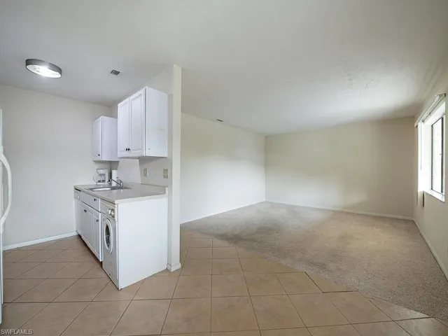 Kitchen featuring washer / clothes dryer, sink, light carpet, and white cabinetry