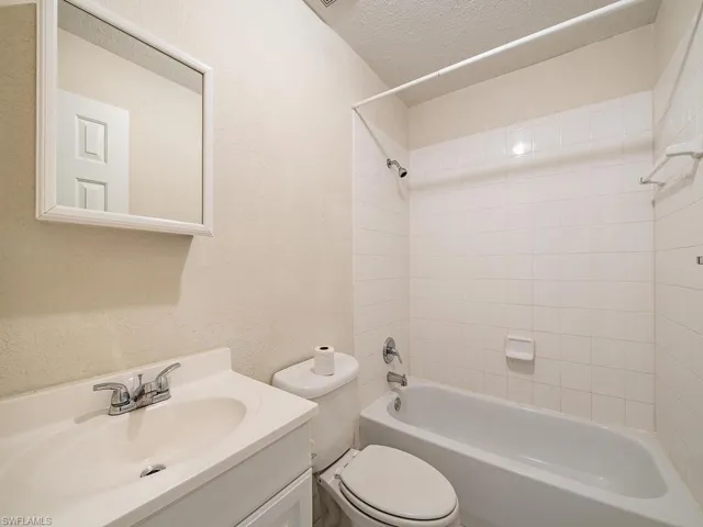 Full bathroom with toilet, tiled shower / bath combo, a textured ceiling, and vanity
