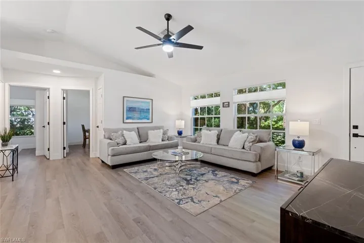 Living room with light hardwood / wood-style flooring, lofted ceiling, ceiling fan, and plenty of natural light