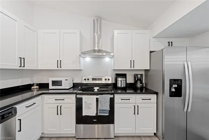 Kitchen with white cabinets, stainless steel appliances, light hardwood / wood-style floors, and wall chimney range hood
