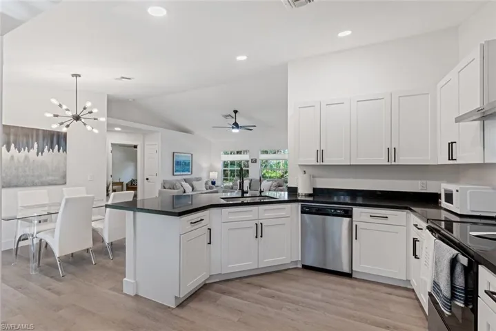 Kitchen with dishwasher, ceiling fan with notable chandelier, light wood-type flooring, and kitchen peninsula