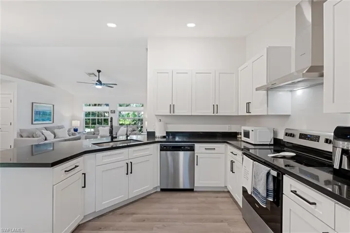 Kitchen with stainless steel appliances, wall chimney range hood, sink, light hardwood / wood-style floors, and ceiling fan