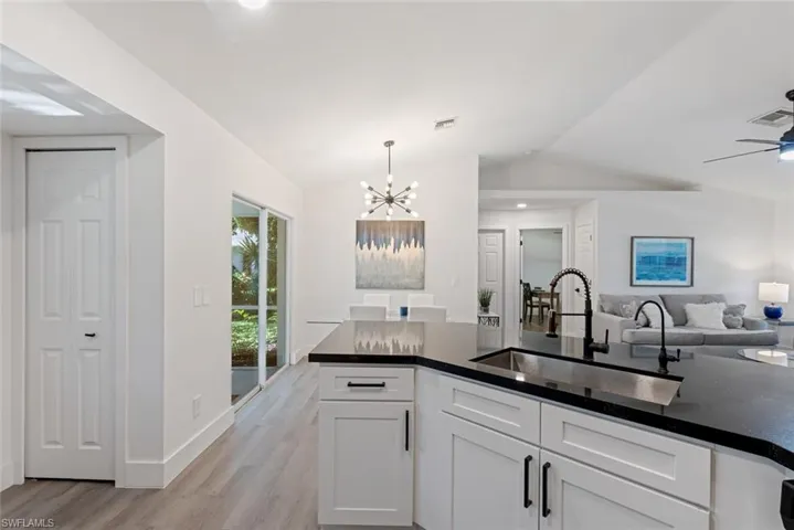 Kitchen featuring light hardwood / wood-style flooring, white cabinets, sink, ceiling fan with notable chandelier, and lofted ceiling