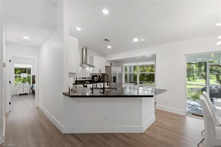 Kitchen with light hardwood / wood-style flooring, stainless steel appliances, kitchen peninsula, white cabinetry, and wall chimney exhaust hood
