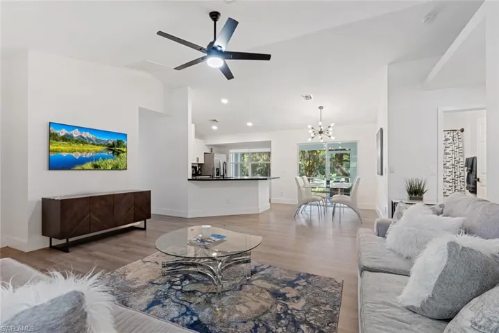 Living room with ceiling fan with notable chandelier and light wood-type flooring