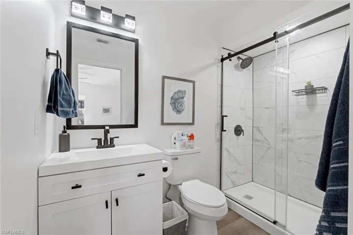 Bathroom with vanity, a shower with door, wood-type flooring, and toilet