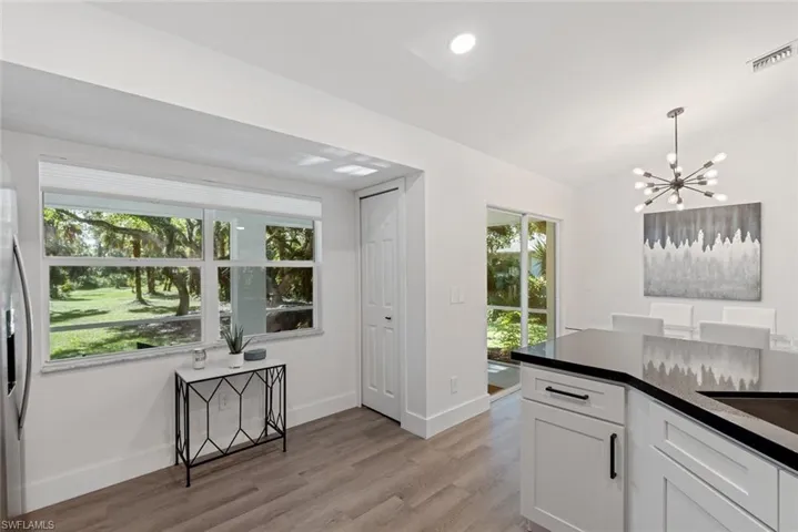 Kitchen with light hardwood / wood-style flooring, vaulted ceiling, hanging light fixtures, white cabinetry, and a chandelier