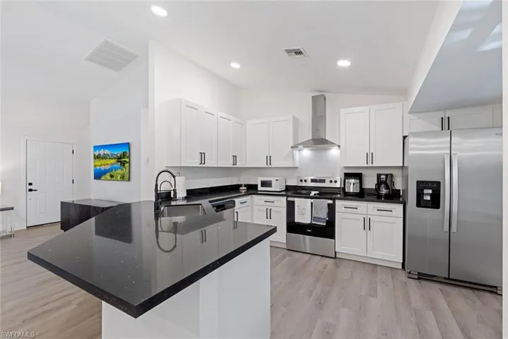 Kitchen featuring light wood-type flooring, kitchen peninsula, wall chimney range hood, stainless steel appliances, and vaulted ceiling