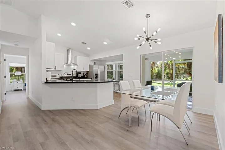 Kitchen with white cabinets, hanging light fixtures, light hardwood / wood-style floors, stainless steel refrigerator with ice dispenser, and wall chimney exhaust hood