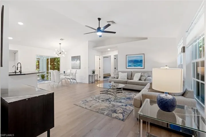 Living room with sink, light wood-type flooring, ceiling fan with notable chandelier, and vaulted ceiling