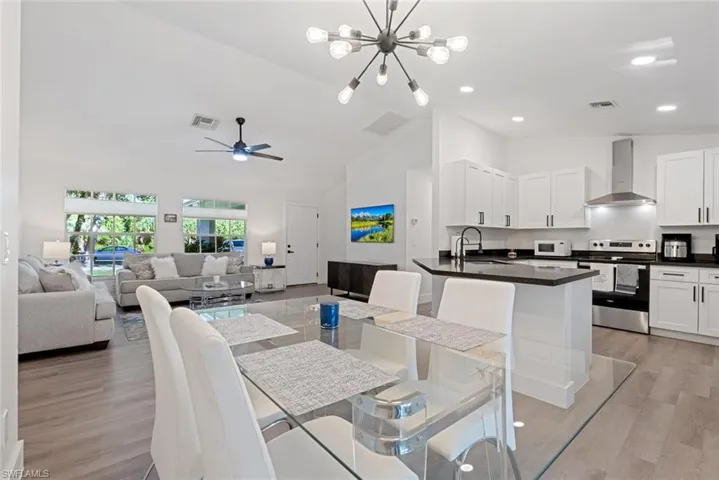Dining room featuring sink, light wood-type flooring, ceiling fan with notable chandelier, and lofted ceiling