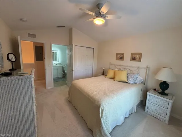 Carpeted bedroom featuring lofted ceiling, electric panel, ensuite bathroom, ceiling fan, and a closet