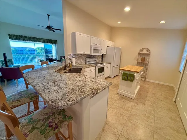 Kitchen with a breakfast bar, white appliances, white cabinets, sink, and kitchen peninsula