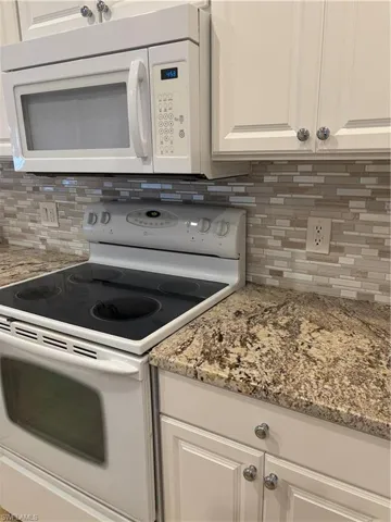 Kitchen featuring backsplash, light stone countertops, white cabinets, and range