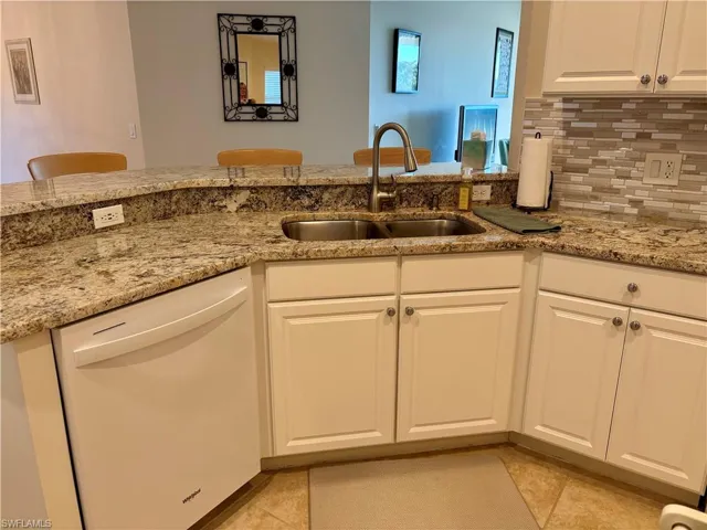 Kitchen featuring sink, kitchen peninsula, white dishwasher, decorative backsplash, and white cabinets