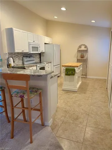 Kitchen featuring sink, a kitchen breakfast bar, light stone counters, kitchen peninsula, and white appliances