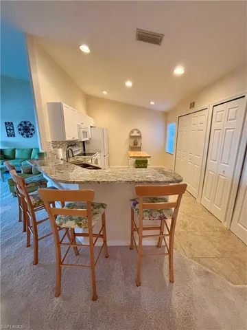 Kitchen featuring white cabinetry, sink, light stone counters, kitchen peninsula, and white appliances