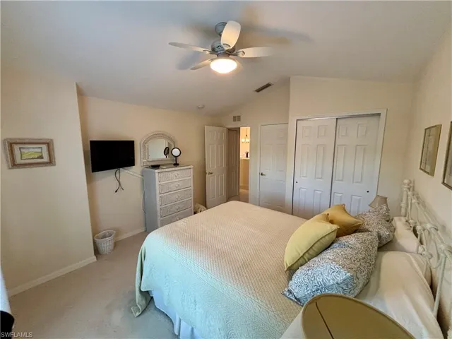 Carpeted bedroom with two closets, ceiling fan, and lofted ceiling