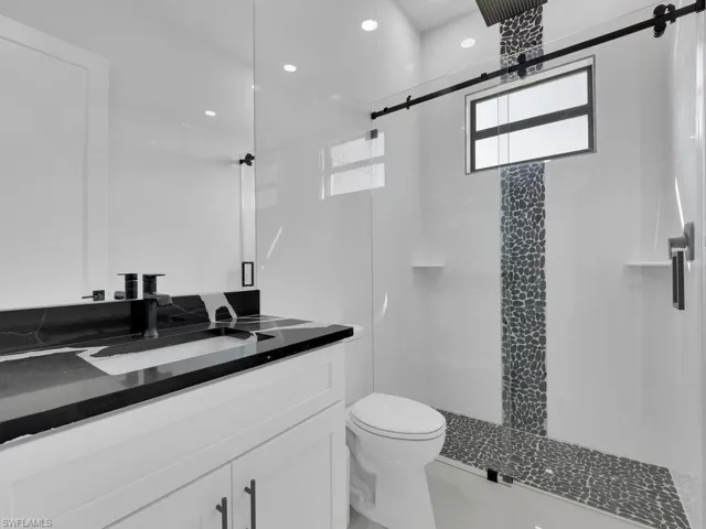 Bathroom featuring a shower with shower door, vanity, and toilet