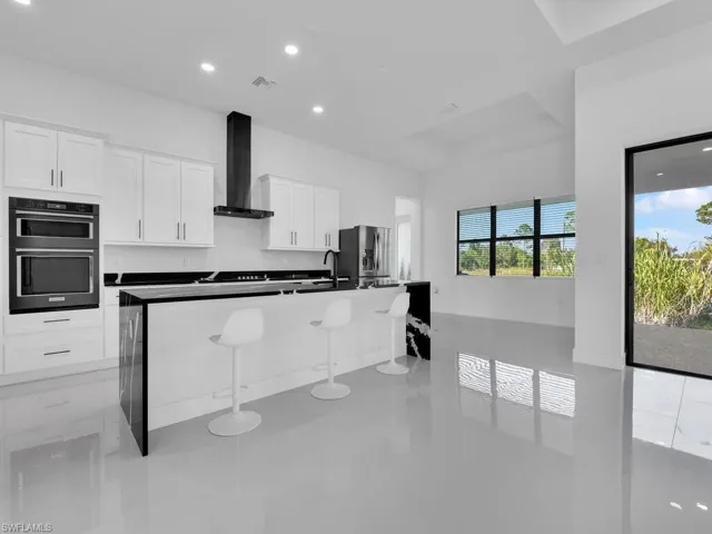 Kitchen with a center island with sink, stainless steel fridge with ice dispenser, a kitchen breakfast bar, white cabinets, and wall chimney exhaust hood