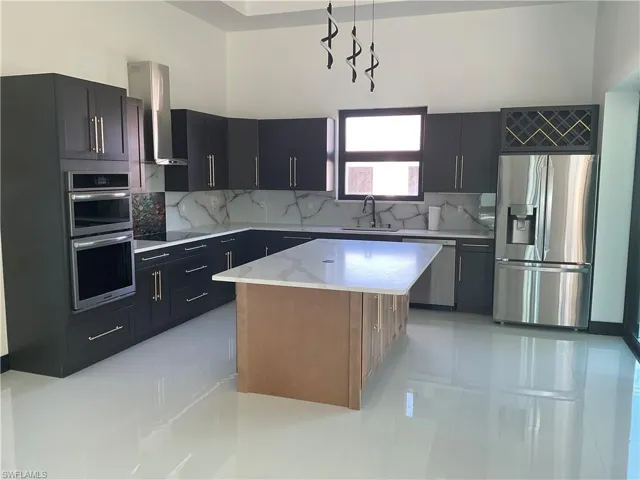 Kitchen featuring dark cabinets, stainless steel appliances, exhaust hood, decorative backsplash, and a high ceiling