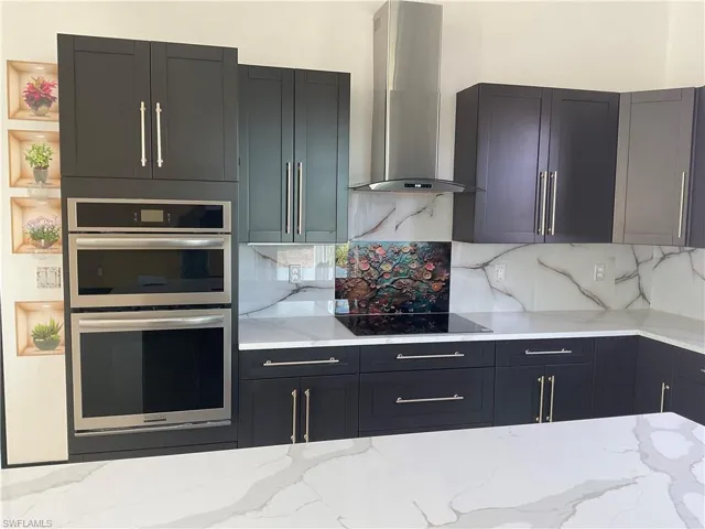 Kitchen featuring stainless steel double oven, light stone countertops, backsplash, and black electric stovetop