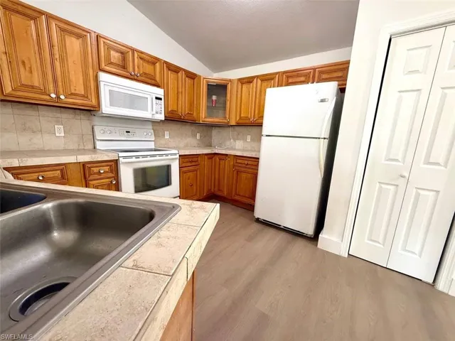 Kitchen featuring backsplash, white appliances, vaulted ceiling, light hardwood / wood-style flooring, and sink