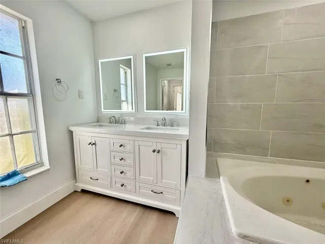 Bathroom featuring hardwood / wood-style flooring, a relaxing tiled tub, and vanity